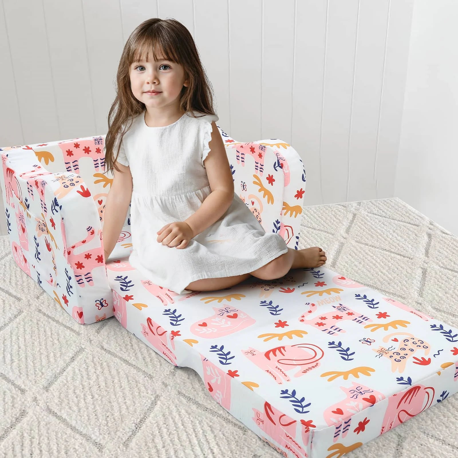 A little girl sitting on an unfolded Glowsofa's Children's fold out sofa with Cat patterns