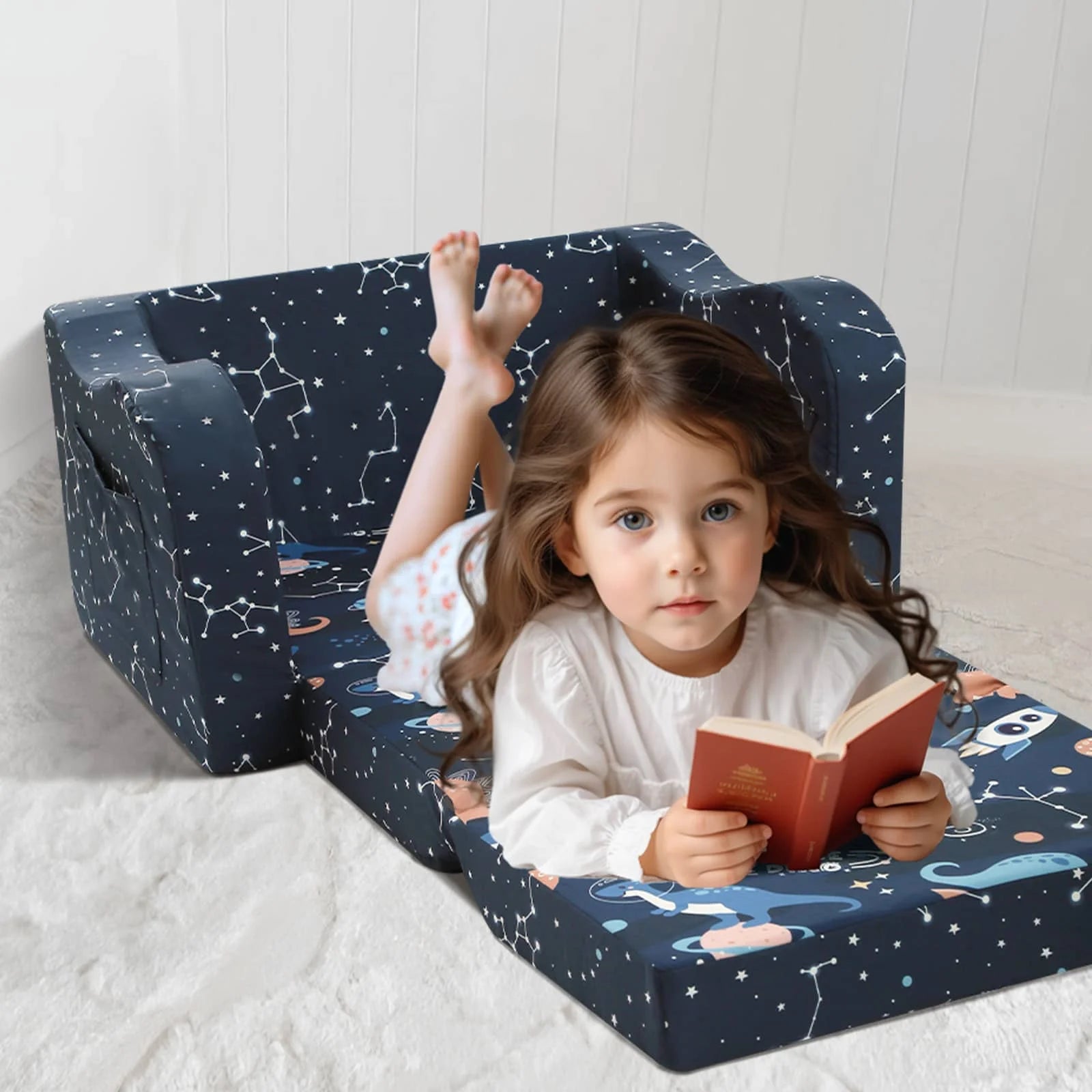 A little girl lying on an unfolded Glowsofa's Children's fold out sofa with Space Dinosaur patterns