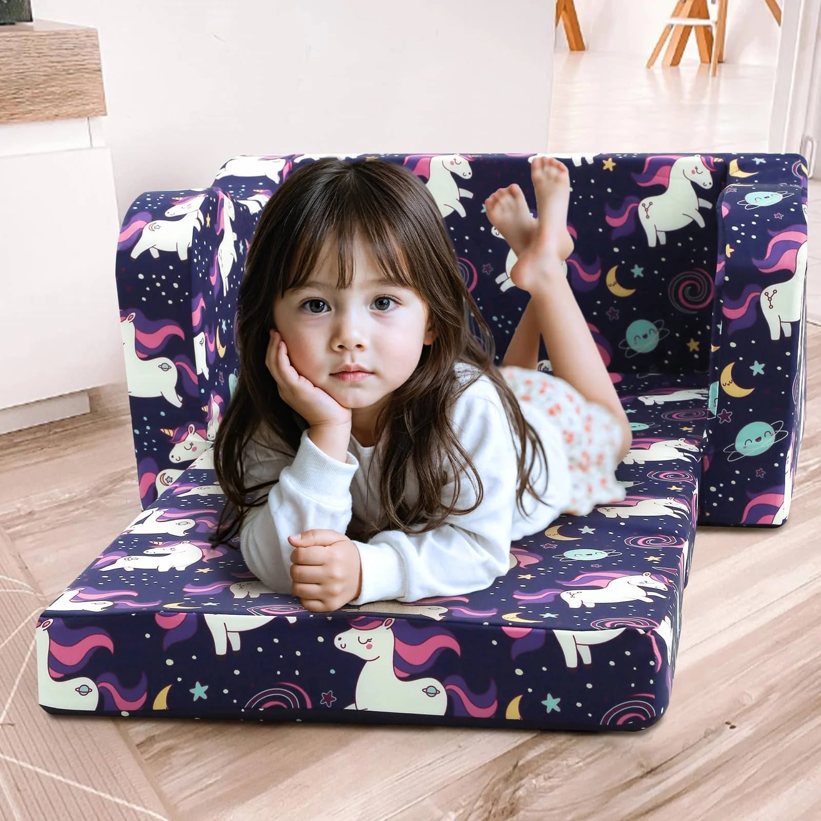 A little girl lying on an unfolded Glowsofa's Children's fold out sofa with Unicorn patterns